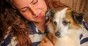 Twix participe au concours pour gagner de l'argent avec cette photo : woman, dog, person, pet, portrait, cuddling, hugging, fluffy, tricolor, white_fur, brown_fur, black_fur, long_hair, curly_hair, bracelets, striped_shirt, indoor, curtain, warm_lighting, affection