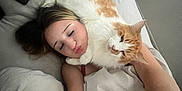 Milo is registered to the contest to win money with this photo: person, cat, bed, blanket, tattoo, pillow, remote_control, white_sheets, orange_cat, lying_down, affection, selfie, indoor, relaxing, cute, pet, sleepy, cozy, human_face, animal