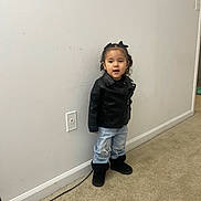Leiliany joined the competition — help win amazing prizes! toddler, child, standing, black_jacket, ripped_jeans, black_boots, curly_hair, indoor, carpet, wall, power_outlet, cable, doorway, expression, person, young_child, casual_clothing, floor, home_interior, cute