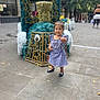 Arlenis joined the competition — help win amazing prizes! toddler, child, dress, blue, white, checkered, shoes, black, sidewalk, urban, sculpture, flower_decor, stars, outdoor, smile, thumbs_up, person, city, daytime, background_people