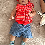 Albert joined the competition — help win amazing prizes! baby, infant, child, hooded_vest, red_clothing, blue_shorts, socks, blanket, floor, lotion_bottle, person, footwear, white_sneaker, indoor, soft_texture, casual_clothing, lying_down, curious_expression, small_hands, cute