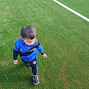 Mohamed Adem participe au concours pour gagner de l'argent avec cette photo : child, boy, sportswear, tracksuit, blue, black, shoes, walking, grass, artificial_turf, outdoor, field, lines, playing, young, casual, active, person, daylight, hair