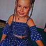 child, girl, smiling, braids, hair_buns, blue_dress, polka_dot, sitting, couch, indoor, necklace, cute, happy, fashion, portrait, young, person, casual, colorful, accessories