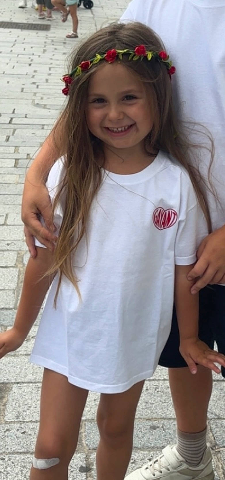 Jade participe au concours pour gagner de l'argent avec cette photo : bandage, casual_clothing, child, cobblestone, flower_crown, footwear, girl, hand, happy, knee, long_hair, outdoor, person, portrait, smiling, sneakers, standing, street, summer, white_tshirt
