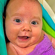 Elaina is registered to the contest to win money with this photo: baby, infant, smiling, blue_eyes, purple_towel, towel, bathtub, bath_time, wet_skin, close_up, portrait, cute, chubby_cheeks, tiny_smile, eyelashes, skin, head, shoulder, happy, playful