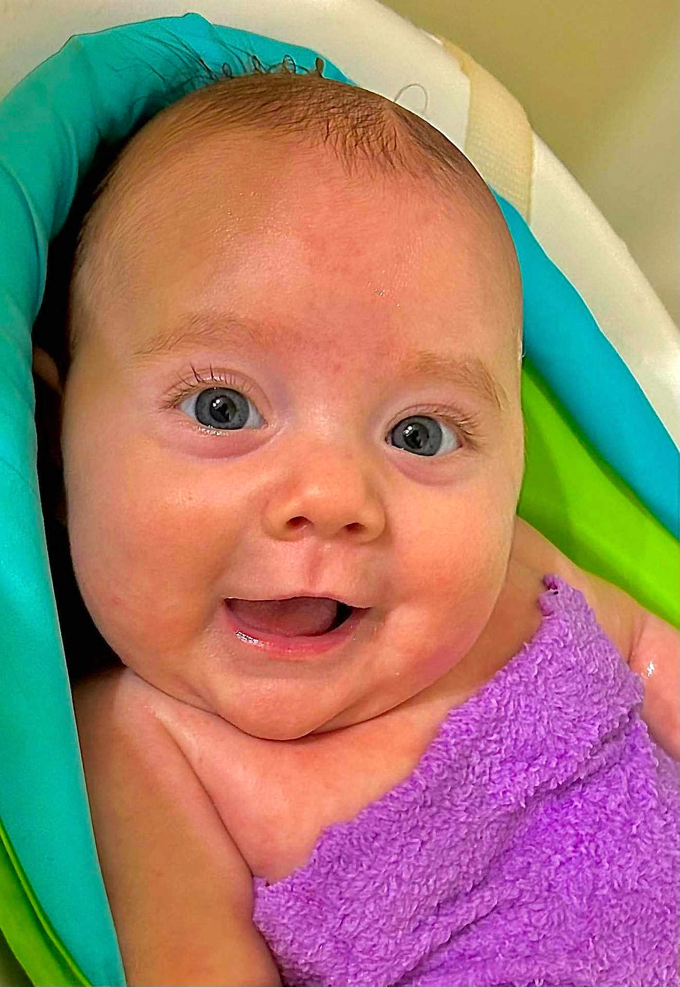 Elaina is registered to the contest to win money with this photo: baby, infant, smiling, blue_eyes, purple_towel, towel, bathtub, bath_time, wet_skin, close_up, portrait, cute, chubby_cheeks, tiny_smile, eyelashes, skin, head, shoulder, happy, playful