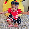 baby, bed, blanket, bow, child, colorful, cute, floral_pattern, headband, indoors, infant, pajamas, person, pikachu, plush, red, sitting, smiling, stuffed_toy, yellow