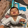 baby, child, playpen, toy, smile, happy, indoor, infant, white_clothing, colorful_toys, mesh_wall, cow_design, blanket, hand, face, young_child, cute, playtime, person, cheerful