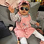 baby, child, sunglasses, pink_dress, headband, bow, pacifier, couch, cushion, toy, hand, footwear, white_tights, indoor, person, clothing, seated, living_room, accessory, cute