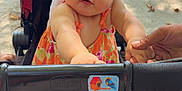 Ava participe au concours pour gagner de l'argent avec cette photo : baby, child, stroller, hand, outdoor, park, bench, sunlight, floral_dress, head_wrap, person, infant, holding_hand, toy, wheel, shadow, pavement, summer, expression, curious