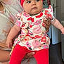 adult_hand, baby, blue_eyes, bow, child, cute, door, expressionless, floor, floral_clothing, furniture, headband, holding, indoor, kitchen_appliance, person, red_leggings, shorts, tie_dye_shirt, wall