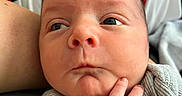 Asher is registered to the contest to win money with this photo: newborn, baby, infant, child, face, portrait, close_up, indoors, blanket, red_blanket, gray_clothing, adult_hand, parent, support, eyes_open, serious_expression, cuddling, bedding, skin, photography