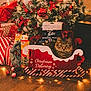 box, cat, christmas_lights, christmas_ornaments, christmas_presents, christmas_tree, cozy, decorations, festive, floor, green, holiday, indoor, pet, pine_cone, red, sleigh, tabby_cat, white, wood_floor