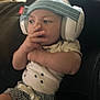 baby, child, headphones, clothing, infant, person, hand, face, sitting, striped_shorts, star_pattern, indoors, fingers, headband, cute, young_child, casual, blurred, comfort, relaxed