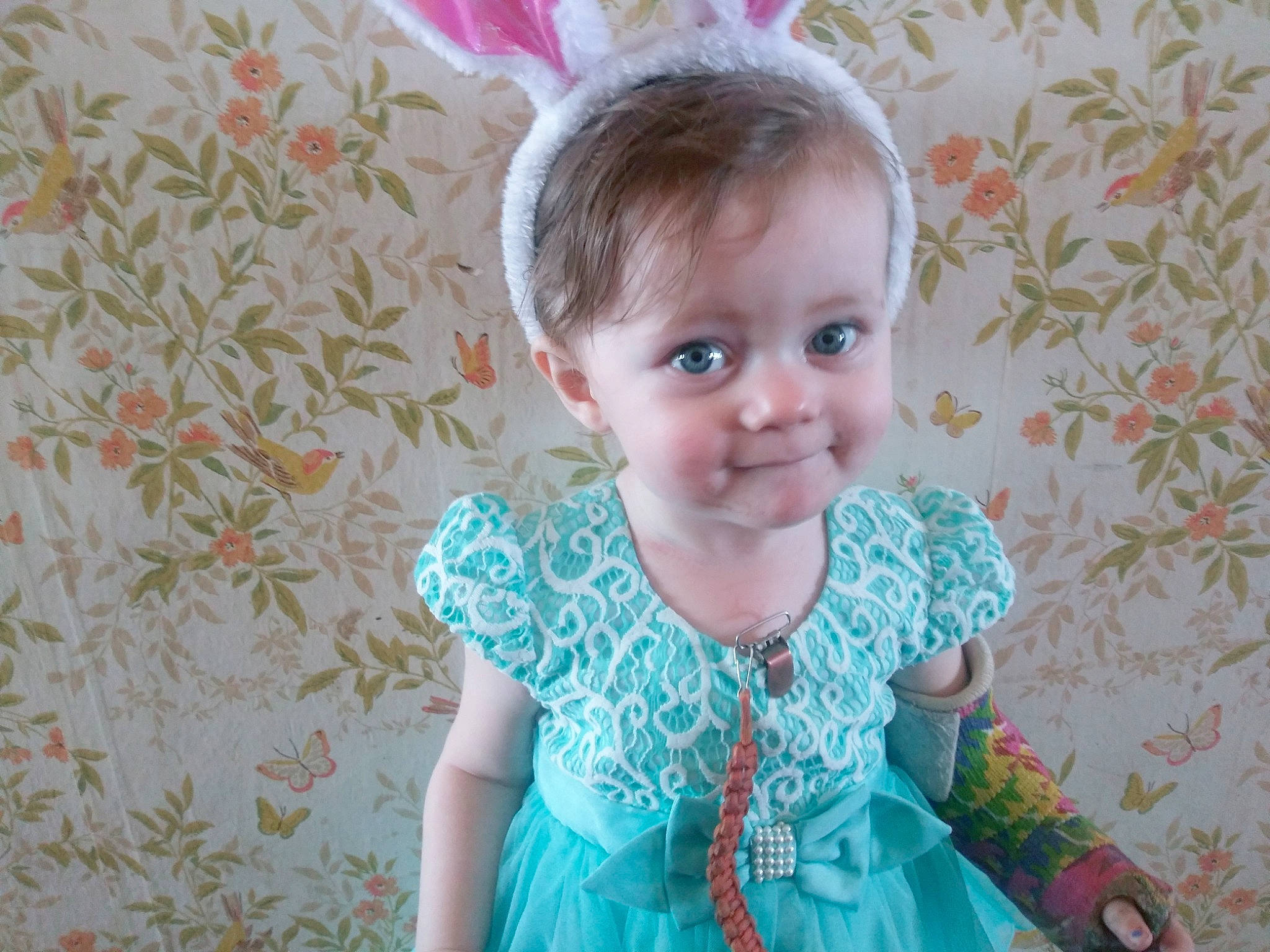 Emiliana is registered to the contest to win money with this photo: baby_toddler_clothing, child, dress, ear, eye, face, fashion_accessory, hair_accessory, head, iris, organ, pattern, person, pink, sleeve, smile, textile, toddler, turquoise