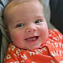 Wyatt is registered to the contest to win money with this photo: baby, smiling, close_up, blue_eyes, orange_clothing, text_on_clothing, infant, happy, face, portrait, cute, child, soft_light, indoor, cozy, skin, person, expression, sitting, young