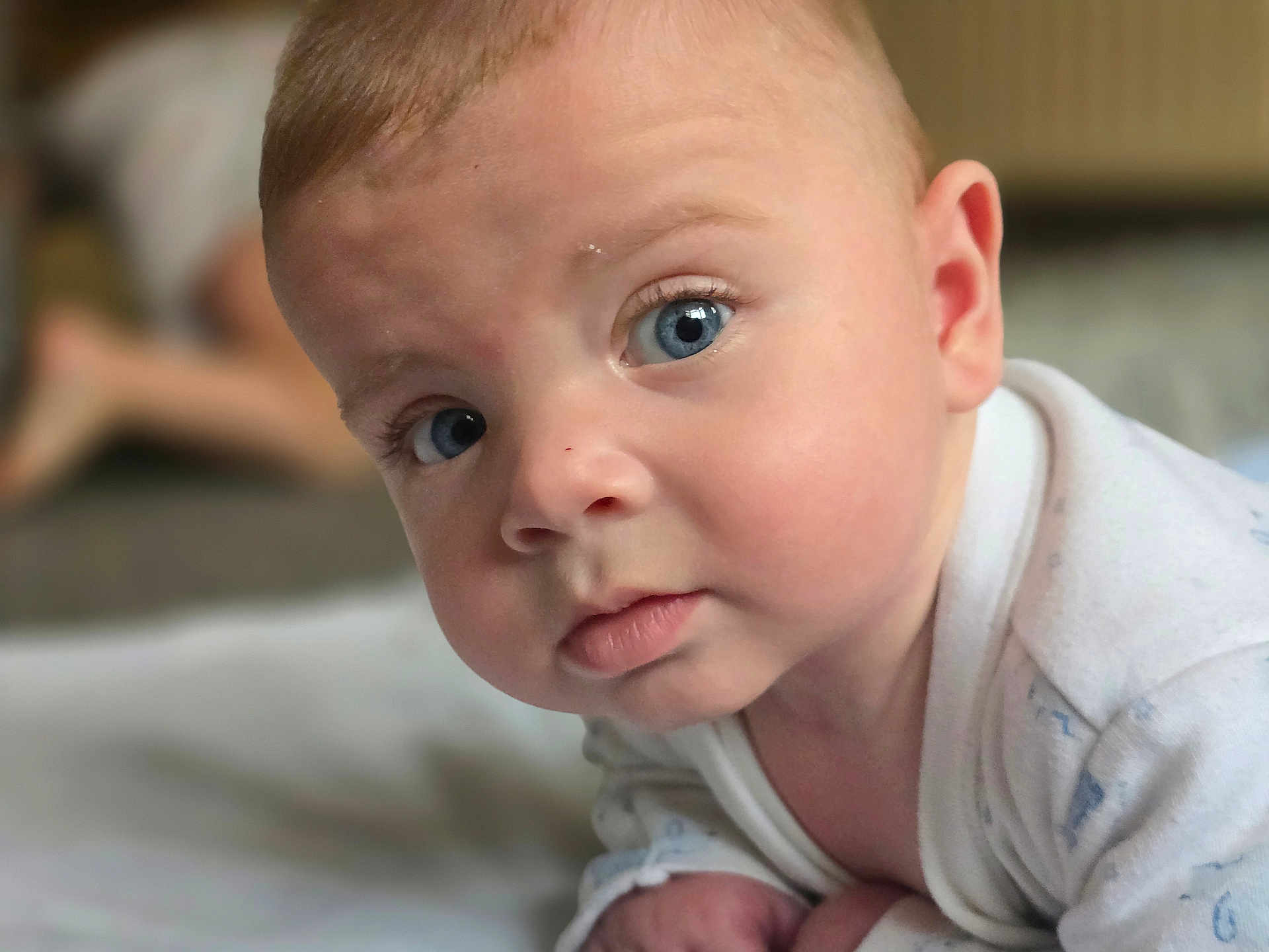Wyatt is registered to the contest to win money with this photo: baby, blue_eyes, close_up, curious, face, infant, indoors, light_skin, looking_at_camera, person, portrait, soft_light, white_clothing, young_child, head, expression, crawling, skin, eyelashes, cheeks