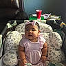 baby, child, pink_dress, headband, playpen, toy, cushion, leather_chair, red_cup, table, word_puzzle_book, blue_wall, indoor, sitting, cute, infant, person, home, furniture, decor