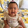 baby, child, smiling, indoor, bed, pillow, clothing, cute, happy, portrait, person, hair_bow, pattern, floral, sitting, infant, young_child, cute_outfit, skin, cheerful