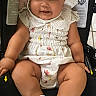 baby, infant, child, car_seat, smiling, white_bonnet, romper, socks, cute, happy, chubby, face, person, seated, indoors, tile_floor, clothing, headwear, skin, legs