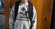 Nico is registered to the contest to win money with this photo: backpack, brown_hair, child, eagles_logo, friendly, full_body, hallway, home, hoodie, indoor, photography, portrait, school_clothing, schoolchild, shorts, smiling, sneakers, standing, wooden_door, young_boy