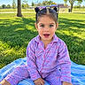 child, girl, toddler, portrait, smiling, outdoor, park, grass, trees, sunlight, sunglasses, pajamas, pink_clothing, blue_blanket, sitting, tablet, playground, daylight, long_hair, happy