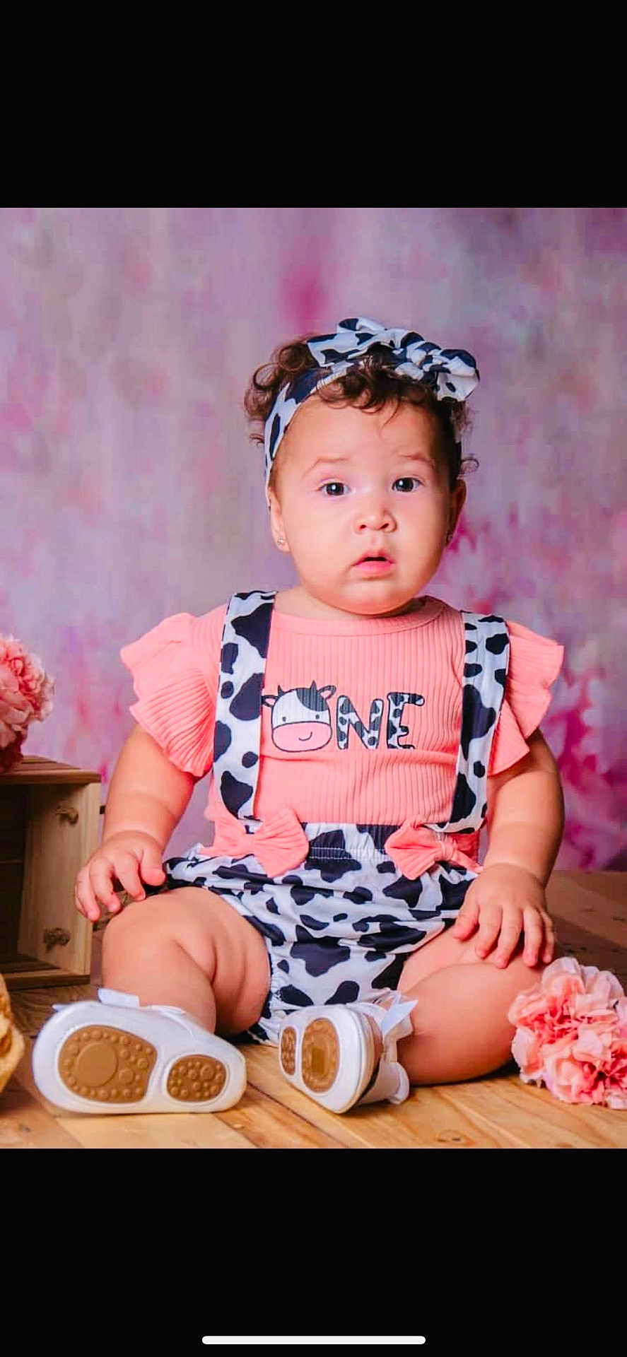 Meghan is registered to the contest to win money with this photo: baby, infant, child, sitting, cow_print, headband, pink, shoes, wooden_floor, flowers, cute, portrait, indoors, clothing, one_year, expression, curious, soft_background, studio, adorable