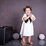 toddler, child, smiling, white_dress, black_bow, curly_hair, sandals, balloon, suitcase, studio, floor_reflection, portrait, happy, clapping, indoor, photography, cute, standing, background, fashion