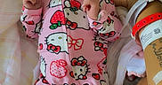 Stormi is registered to the contest to win money with this photo: baby, infant, child, portrait, lying_down, pink_onesie, hello_kitty, headband, bow, floral_bedding, blanket, hospital_bracelet, adult_arm, indoor, bed, cozy, serious_expression, hands, fashion, photography