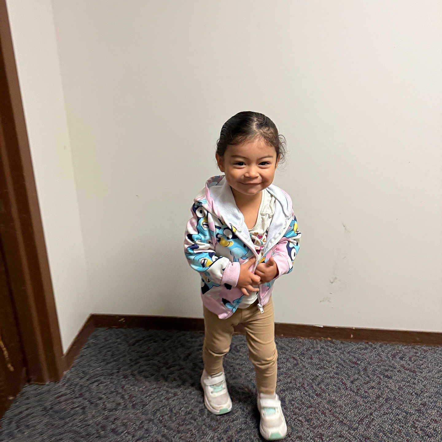Sophia is registered to the contest to win money with this photo: beige_pants, carpet, casual_wear, child, colorful_clothing, cute, doorframe, face, happy, hoodie, indoor, person, playful, portrait, smile, standing, toddler, wall, white_sneakers, young_child