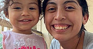 Sophia is registered to the contest to win money with this photo: toddler, child, woman, smile, outdoor, porch, bib, toy, plush, happy, face, person, casual_clothing, daylight, family, portrait, cute, funny_text, young_child, natural_light