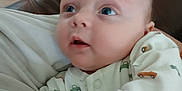 Liam is registered to the contest to win money with this photo: baby, infant, onesie, car_pattern, face, eyes, hand, indoor, furniture, playpen, couch, person, child, cute, soft, portrait, cozy, home, wood_floor, blanket