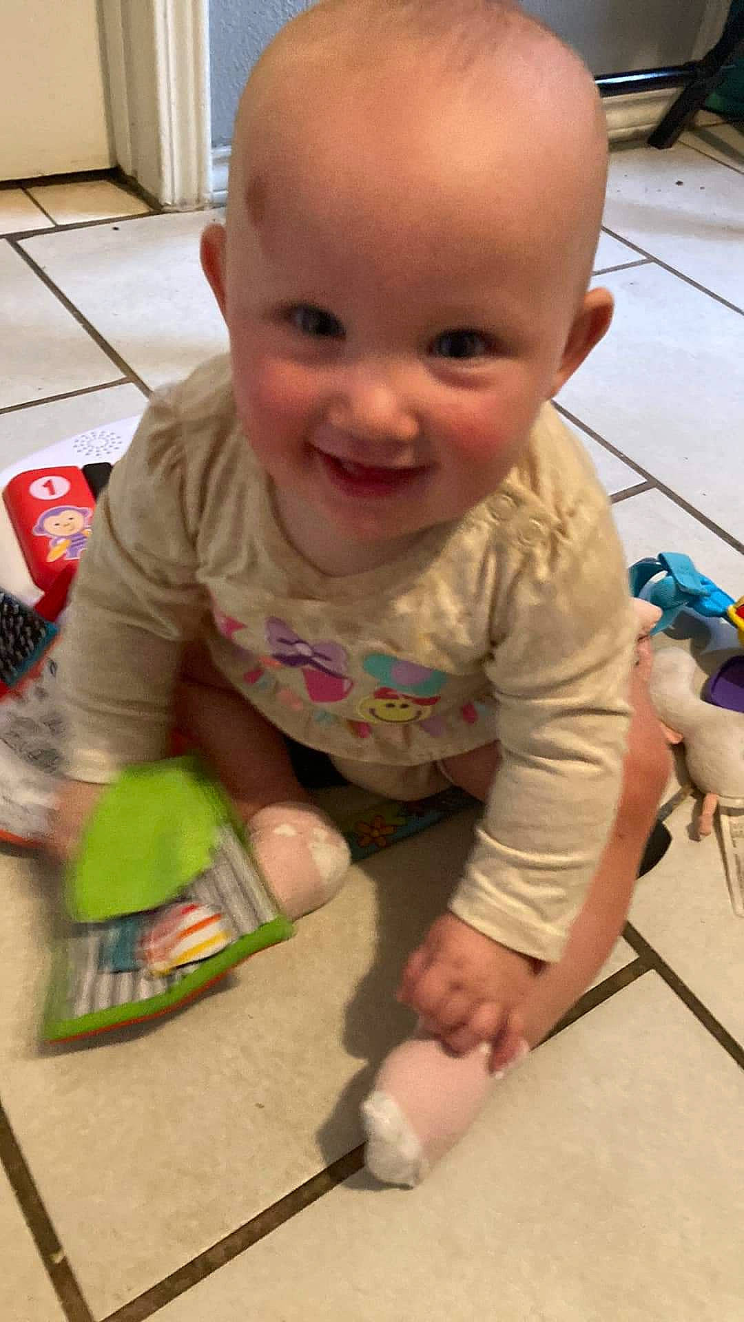 Genesis is registered to the contest to win money with this photo: baby, baby_toddler_clothing, cheek, child, eye, finger, floor, flooring, foot, fun, hardwood, head, human_body, joy, person, play, sitting, skin, smile, toddler