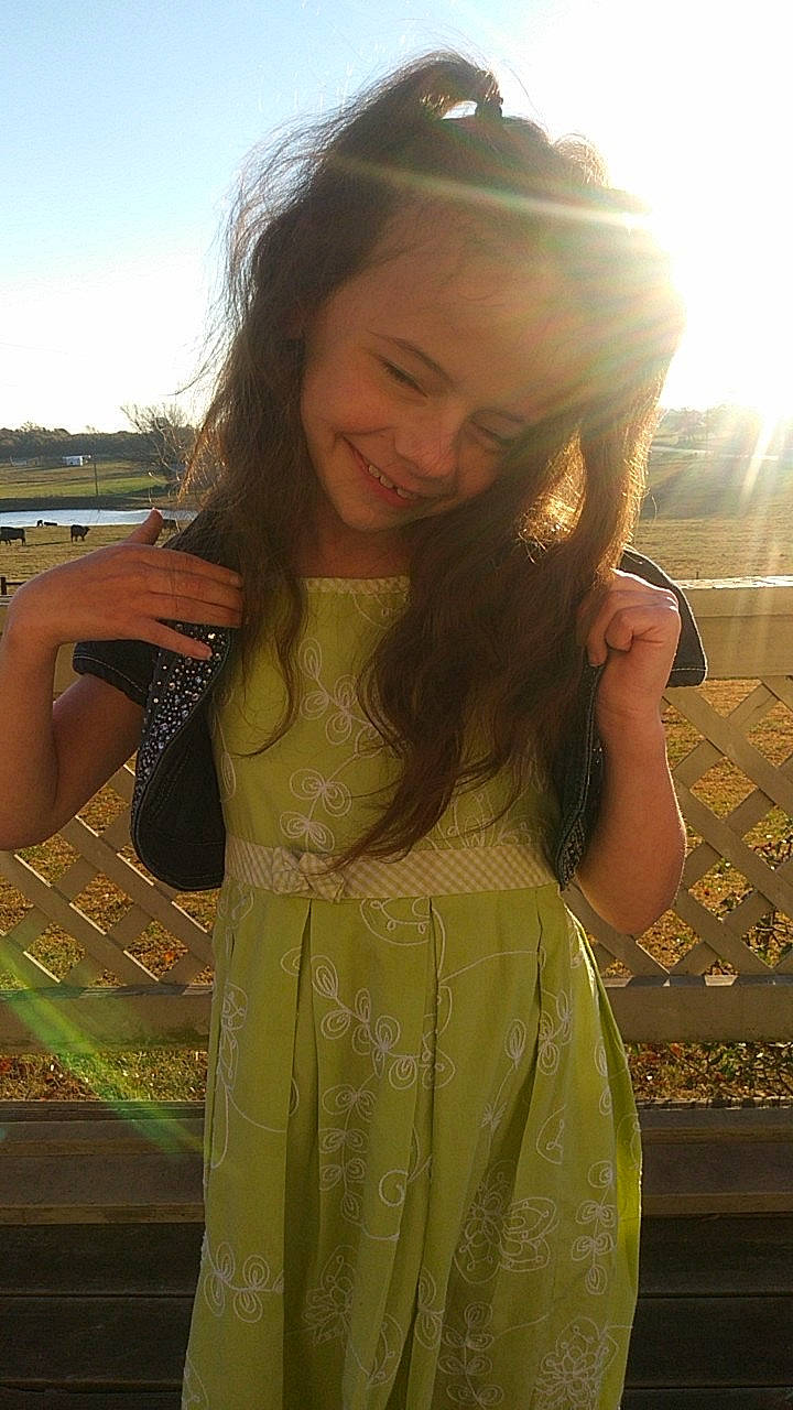 Emalee is registered to the contest to win money with this photo: arm, dress, facial_expression, flash_photography, gesture, grass, hairstyle, hand, happy, joint, joy, light, lip, neck, person, plant, shoulder, skin, sky, sleeve