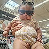 baby, child, infant, sunglasses, fashion, store, retail, shopping, held, portrait, indoor, clothing, patterned_outfit, topknot, serious_expression, face, hands, merchandise, baby_apparel, funny