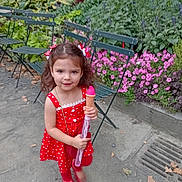 Alanna joined the competition — help win amazing prizes! child, girl, red_dress, toy_ice_cream, bubble_wand, park, flowers, green_chairs, outdoor, playful, cute, smiling, nature, leafy, sidewalk, summer, happy, young, casual, daylight