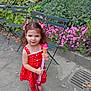child, girl, red_dress, toy_ice_cream, bubble_wand, park, flowers, green_chairs, outdoor, playful, cute, smiling, nature, leafy, sidewalk, summer, happy, young, casual, daylight
