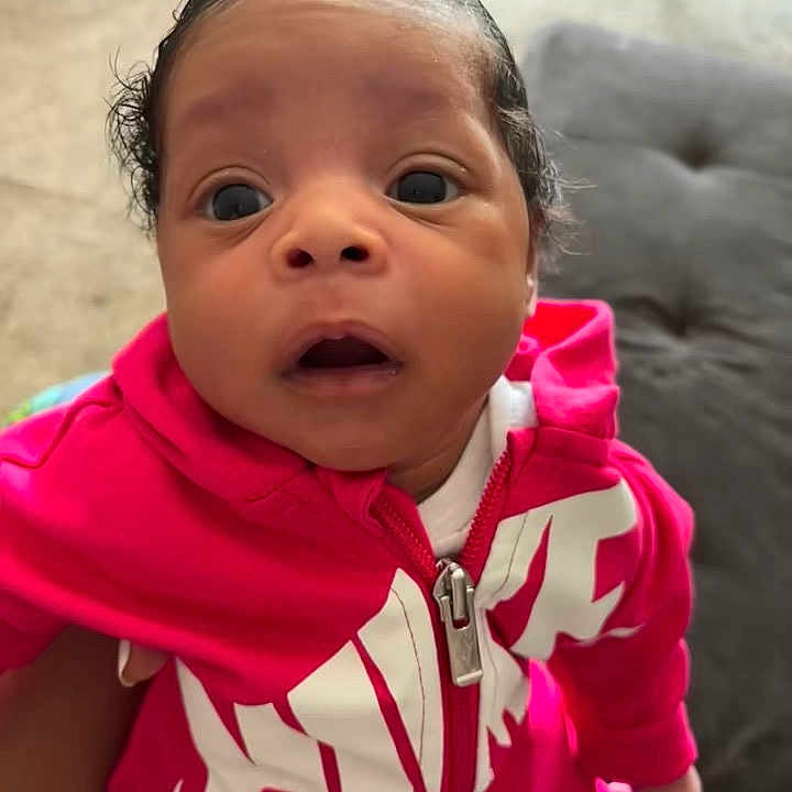 Jahmaika is registered to the contest to win money with this photo: baby, child, hoodie, pink_clothing, face, portrait, indoor, person, young_child, expression, curious, sitting, cute, infant, human, apparel, closeup, eyes, head, love