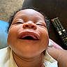 baby, child, closeup, clothing, couch, expression, face, hair, happy, head, infant, joy, living_room, mouth, person, remote_control, skin, smile, teeth, white_outfit