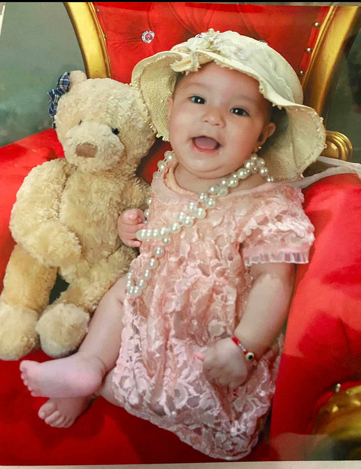 Evany is registered to the contest to win money with this photo: baby, teddy_bear, red_chair, pink_dress, lace, hat, pearl_necklace, bracelet, smile, happy, child, plush_toy, indoor, portrait, cute, sitting, furniture, accessories, person, decor