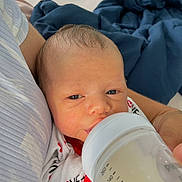 Luis joined the competition — help win amazing prizes! baby, newborn, bottle, feeding, infant, person, hand, clothing, blanket, arm, indoor, milk, onesie, love, face, head, sleepy, closeup, comfort, care