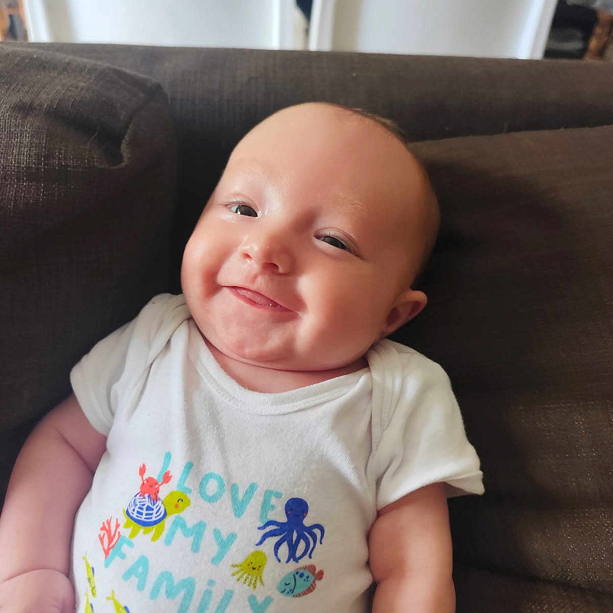 Eden a rejoint le concours — aidez-le/la à gagner de superbes lots ! baby, cheeky, child, couch, crab, cute, family, fish, happy, indoors, infant, octopus, portrait, relaxed, sea_creatures, smiling, text_on_clothing, turtle, whale, white_onesie