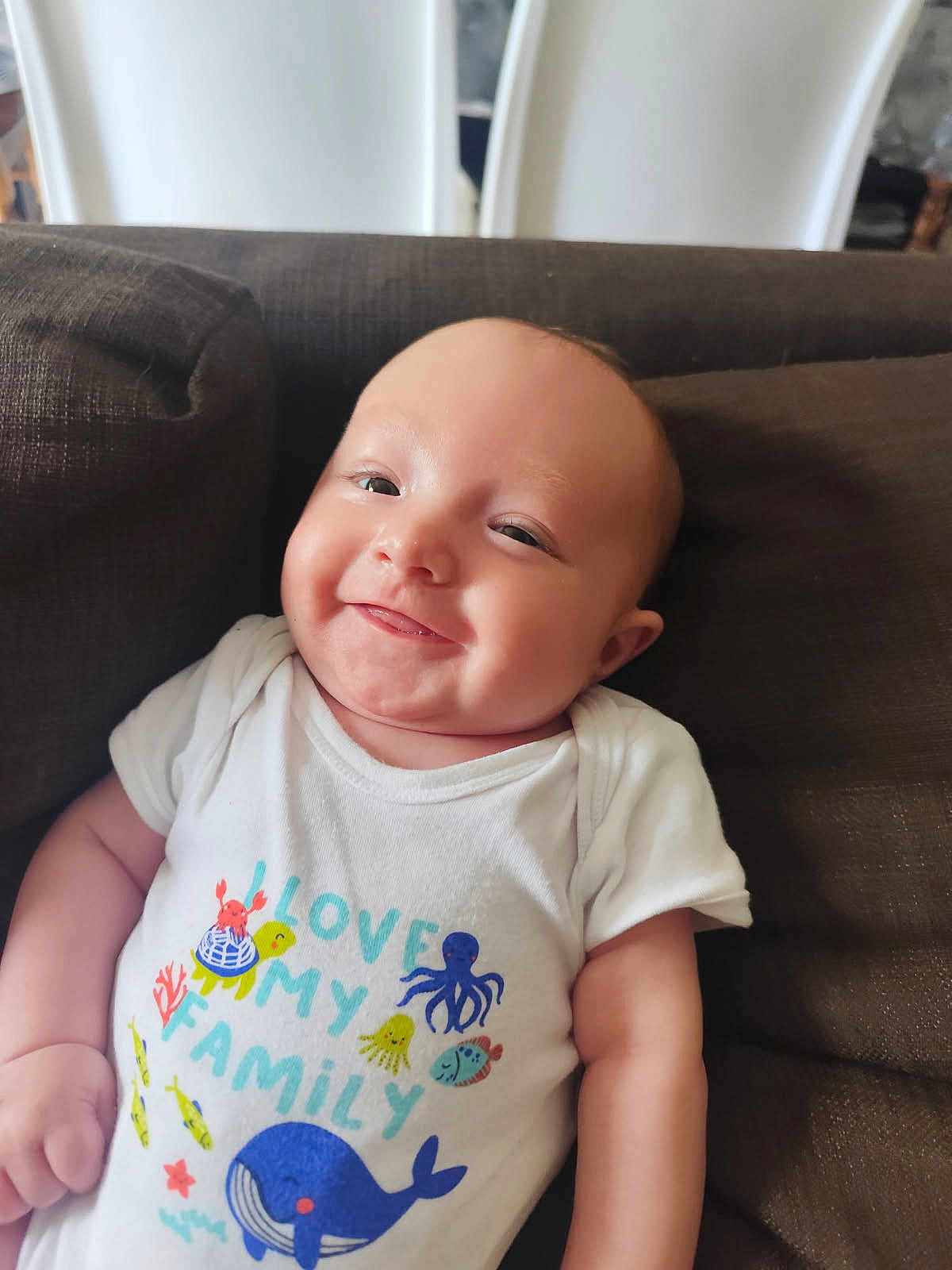 Eden a rejoint le concours — aidez-le/la à gagner de superbes lots ! baby, infant, smiling, couch, white_onesie, text_on_clothing, sea_creatures, turtle, whale, octopus, fish, crab, happy, cheeky, cute, child, indoors, portrait, relaxed, family