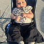 Myra is registered to the contest to win money with this photo: baby, child, shopping_cart, seat, headband, clothing, socks, outdoor, sunlight, pavement, black_pants, beige_top, embroidery, face, hands, footwear, person, sitting, daylight, shopping