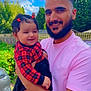 Myra is registered to the contest to win money with this photo: baby, child, man, adult, smiling, holding, outdoor, daylight, sky, clouds, trees, greenery, fence, car, plaid_clothing, red_clothing, pink_shirt, beard, hair_clips, happy