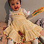 toddler, child, yellow_dress, pom_poms, blue_bow, toy, rainbow_colored, white_tights, unicorn_blanket, bed, smiling, happy, indoor, playtime, cute, sitting, person, face, clothing, hair_bow