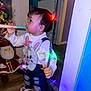 toddler, child, indoor, christmas_lights, holiday, toy, bunny_bib, jeans, ripped_jeans, whisk, face, person, floor, wooden_floor, santa_doll, decorations, colorful_lights, curious, standing, holiday_season