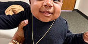 Airess is registered to the contest to win money with this photo: baby, child, smiling, portrait, indoor, necklace, black_clothing, hand, person, face, cute, happy, jewelry, carpet, door, furniture, holding, skin, expression, young