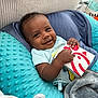 baby, smiling, infant, blue_pillow, blanket, pacifier, chickfila_box, indoor, cute, happy, clothing, child, relaxed, portrait, soft_texture, furniture, home, comfort, hand, face