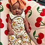 baby, infant, bow, headwear, floral_outfit, blanket, cherry_pattern, smile, cute, child, clothing, sitting, face, hands, feet, indoors, soft_texture, colorful, portrait, young
